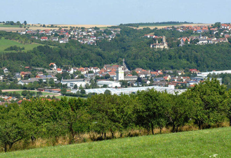 From the distance you can see Krautheim from a hill. In front of it you can see trees and a meadow. Behind it are two villages.