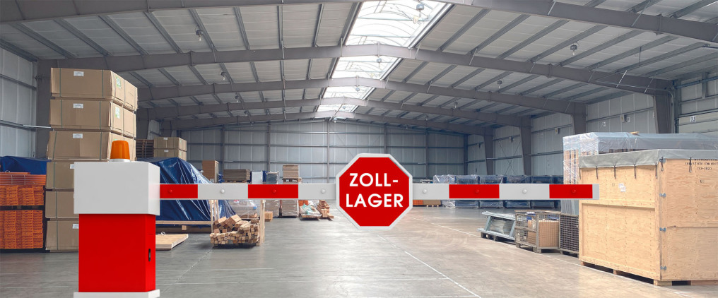 One looks into the rear part of a newly built warehouse. In the front part of the picture there is a barrier with a STOP traffic sign, but with the words ZOLL-LAGER (... customs warehouse). Behind the barrier you can see a lot of goods.