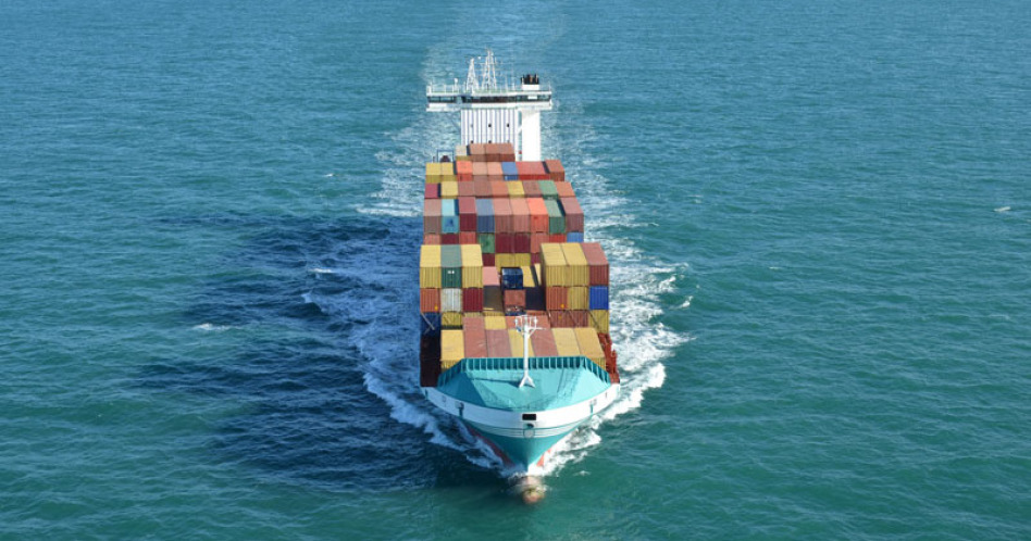 Ein großes Containerschiff fährt auf dem offenenen Meer auf den Betrachter zu. Es ist eine Luftaufnahme.
